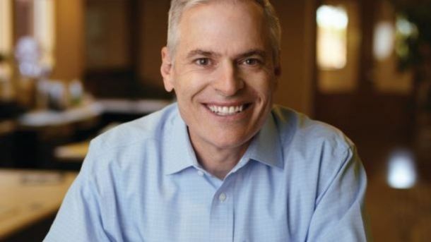 Sorriso caloroso de um homem de cabelos grisalhos vestindo uma camisa azul clara, em um ambiente de escritório, representando Patrick Lencioni, um facilitador de 'conversas difíceis com sua equipe