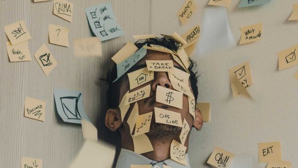 Homem com cabeça encostada na parede e o rosto coberto por post-its, indicando intenso trabalho emocional